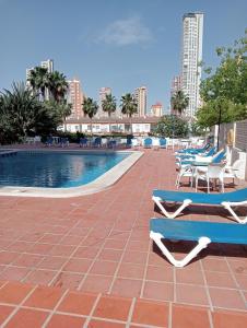 a swimming pool with chairs and a table next to a building at luxmar beach in Benidorm