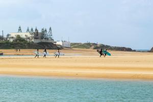 a group of surfers walking on the beach with their surfboards at Surf house apartment in Oualidia