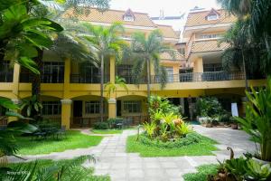 a large yellow building with palm trees in the courtyard at Piman Garden Boutique Hotel in Khon Kaen