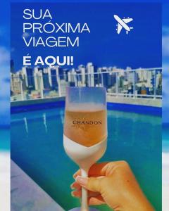 una mano che tiene un bicchiere di vino di fronte a una piscina di Flat Lindíssimo Beira-Mar a Salvador