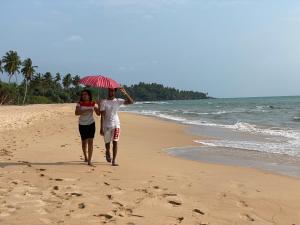 un homme et une femme se promenant sur la plage avec un parasol dans l'établissement Sri Palms, à Kosgoda