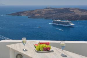 a plate of fruit and wine glasses on a table with a cruise ship at The Last Sunbeam - Adults Only in Fira