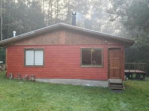 a red cabin with a window and a door at CABAÑA ENTRE ARRAYANES Y COPIHUES Selva VALDIVIANA in Valdivia