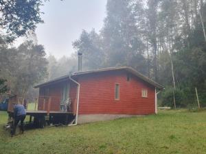 a red house with a man standing in front of it at CABAÑA ENTRE ARRAYANES Y COPIHUES Selva VALDIVIANA in Valdivia