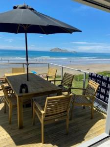 a wooden table and chairs with an umbrella on the beach at Ultimate Beach Front in Waimarama