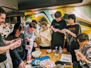 eine Gruppe von Menschen, die um einen Tisch stehen und Essen zubereiten in der Unterkunft R Hostel Namba south in Osaka