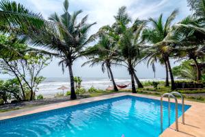a swimming pool with palm trees and the ocean at Amadi Beach Front Resort in Mandrem