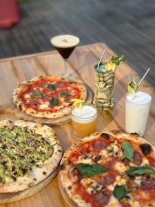 drei Pizzen auf einem Holztisch mit Getränken in der Unterkunft The Penida Project in Nusa Penida