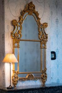 un espejo de oro en una pared junto a una lámpara en gîte ou chambres d'hôtes au château de Montclair, en Pommiers