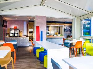 um restaurante com mesas brancas e cadeiras coloridas em Ibis budget Issoire em Issoire