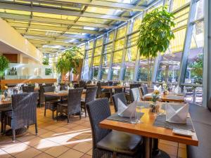 a restaurant with wooden tables and chairs and windows at Mövenpick Hotel München-Airport in Hallbergmoos