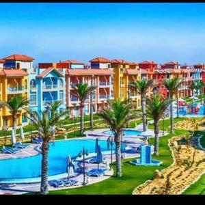 a resort with a pool and palm trees and buildings at Porto Matroh New Chalets in Marsa Matruh