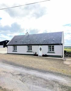 une maison blanche avec un toit noir sur une route dans l'établissement Hilltop Cottage, à Kilkee