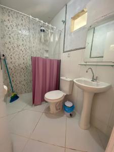 La salle de bains est pourvue d'un rideau de douche rose, de toilettes et d'un lavabo. dans l'établissement Pousada Raio de Sol - Ilha de Itaparica- Catu á 150 m da praia, à Vera Cruz de Itaparica