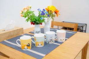 Una mesa con cuatro tazas de café y flores. en Guest House HARU DREAM ABENO HOUSE, en Osaka