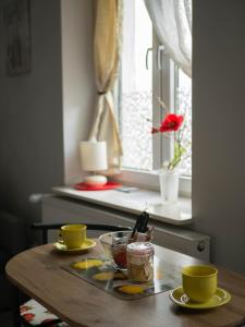 une table en bois avec deux tasses jaunes et une fenêtre dans l'établissement Apartament przy synagodze, à Przemyśl
