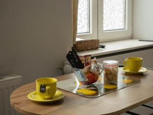 une table avec deux tasses jaunes et un plateau de nourriture dans l'établissement Apartament przy synagodze, à Przemyśl