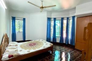 a bedroom with a bed with blue curtains and a fan at Kumar Para Deluxe Villa in Sylhet