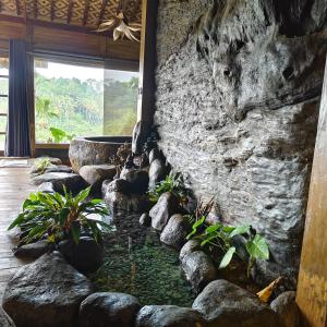a stone wall with a pond in a room with plants at Beyond Heaven in Tampaksiring