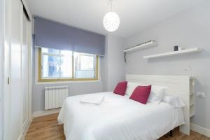 a bedroom with a white bed with two red pillows at Con parking gratis en el centro by CABANA Rentals in Vigo