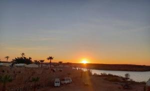 a sunset with two cars parked next to a body of water at Nilehouse in Abu Simbel