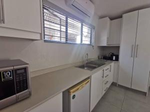 a white kitchen with a sink and a microwave at Kingfisher Cottage in Ballito
