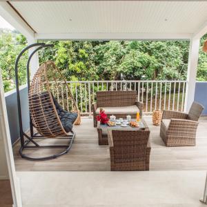 a porch with a swing and chairs and a table at Villa F4 chic avec jacuzzi en Martinique in Le Lamentin