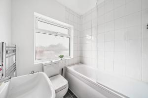a white bathroom with a tub and a toilet and a window at 3-Bed, Sleeps 6, Near M1/M62 in Morley