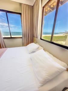 a bedroom with a bed and two windows with the ocean at Itacimirim Apartments Boulevard e Ondas in Itacimirim