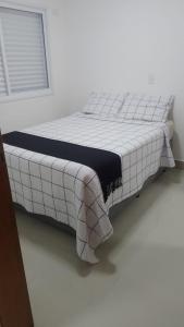 ein Bett in einem weißen Zimmer mit einer Decke darauf in der Unterkunft CASA SETE ENSEADA AR COND Suíte E ESTACIONAMENTO GRÁTIS e uma ótima localização na enseada in Guarujá