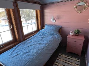 a bedroom with a bed with a blue comforter and two windows at Koselig feriehus sentralt i Sirdal in Tjørhom