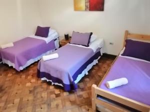 three beds in a room with purple sheets at Hotel Baleares in Santiago