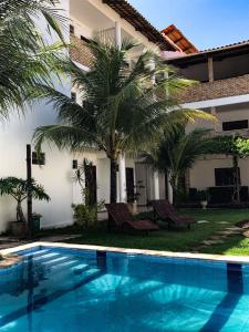 a swimming pool in front of a house with palm trees at Hospedaria Cumbuco - Kitnets Completas in Caucaia