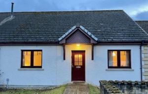 a white house with a black roof and a red door at Taigh Munro in Aviemore