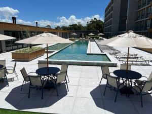 einen Pool mit Tischen, Stühlen und Sonnenschirmen in der Unterkunft Resort com Piscina Aquecida e Garagem em Xangri-lá in Xangri-lá