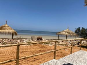 Mouamla的住宿－Beach houses Lost paradise，海滩上有两个稻草伞和大海