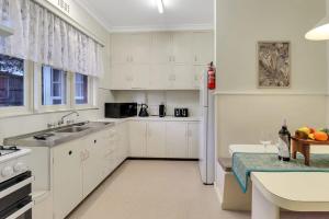 a kitchen with white cabinets and a table with a bowl of fruit at GATSBY walk to Geelong CBD and Waterfront in Geelong