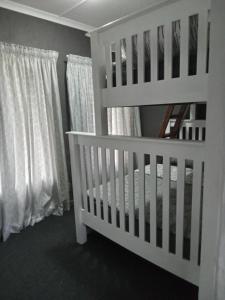 - un lit bébé blanc dans une chambre dotée de rideaux blancs dans l'établissement Howick Greendale 4 Self Catering Units Solar & Battery Back-Up, à Howick