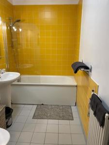 La salle de bains est pourvue de carrelage jaune, d'une baignoire et d'un lavabo. dans l'établissement Appartement spacieux Gentilly, à Gentilly