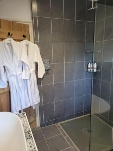 ein Badezimmer mit einer Dusche und weißen Bademänteln auf einem Kleiderständer in der Unterkunft Honeysuckle Cottage Annex with hot tub near Needham Market in Needham Market