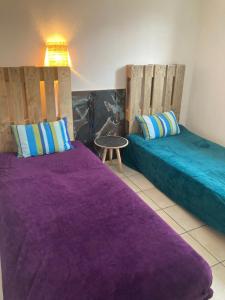two beds in a room with purple sheets and a table at Sérénité in Biscarrosse