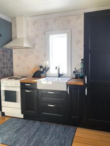 eine Küche mit schwarzen Schränken, einem Waschbecken und einem Fenster in der Unterkunft Villa Stuga in Hammarstrand