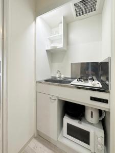 eine weiße Küche mit einer Spüle und einer Mikrowelle in der Unterkunft bHOTEL Yutori - 1Br Apartment in Onomichi City near the Station in Onomichi
