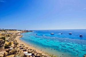 a beach with umbrellas and people in the water at Sharm Best Holiday in Sharm El Sheikh