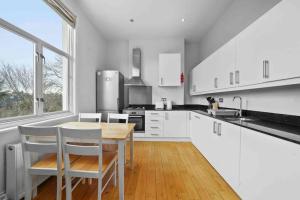 a kitchen with white cabinets and a table and chairs at Queen’s Park, Spacious 3 Bedroom Flat in London