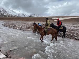 un grupo de personas montando caballos a través de un río en Alay Travel house, en Sary-Mogul