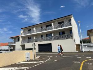 two people crossing a street in front of a building at Très bel appartement neuf - Parking et Terrasse in Biscarrosse