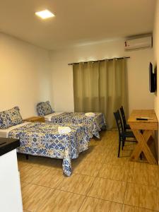 a room with two beds and a table and a desk at Hospedaria Cumbuco - Kitnets Completas in Caucaia