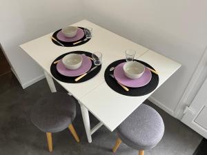 une table blanche avec des assiettes, des chapeaux et deux chaises dans l'établissement Charmante maison de ville, à Arnouville-lès-Gonesse