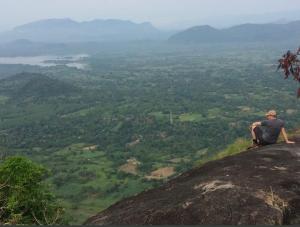 Ein Mann, der auf einem Felsen sitzt und ein Tal ansieht. in der Unterkunft Charitha Rest in Ampara